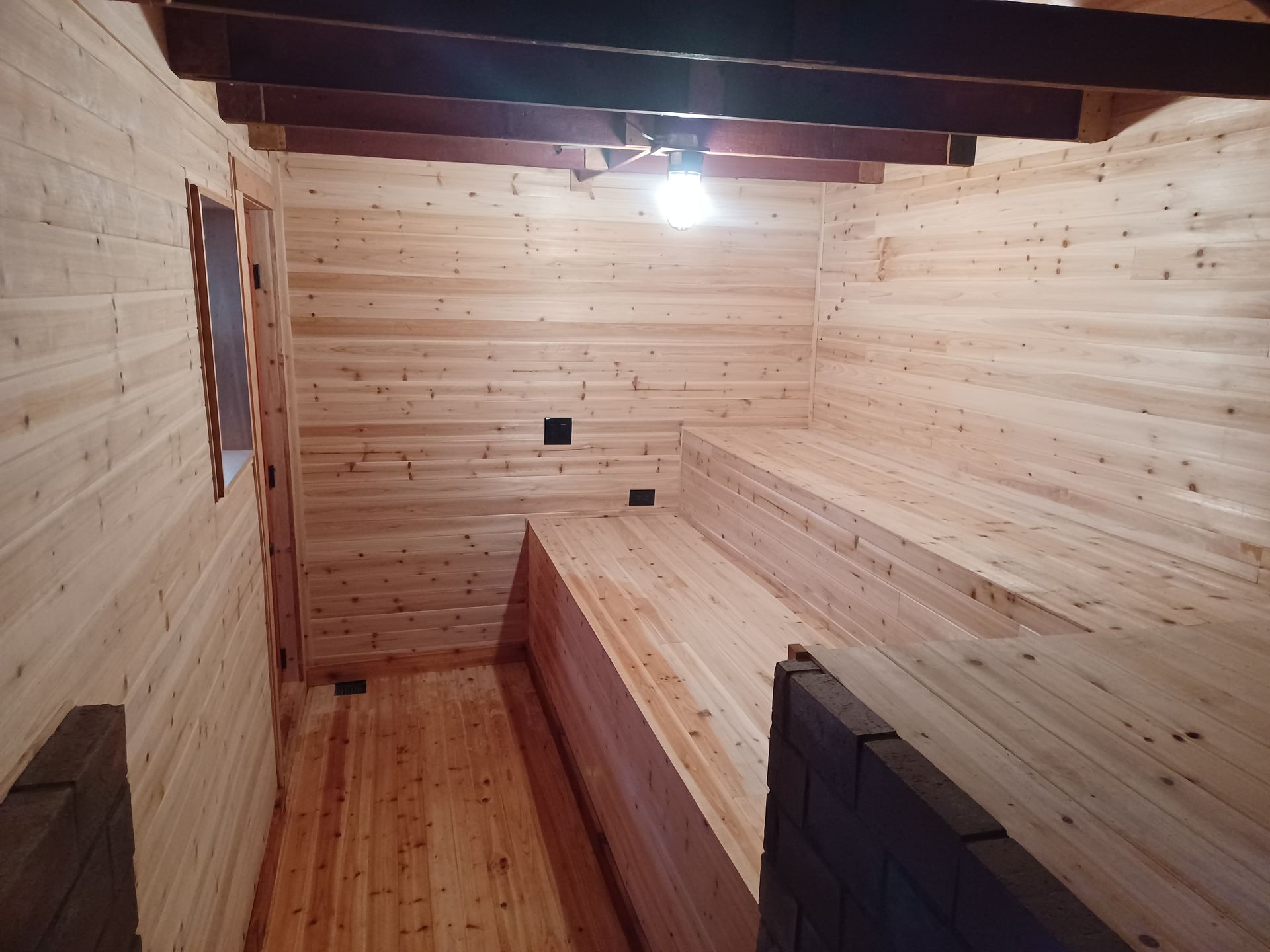 Wood-paneled sauna room with bench seating and a single overhead light