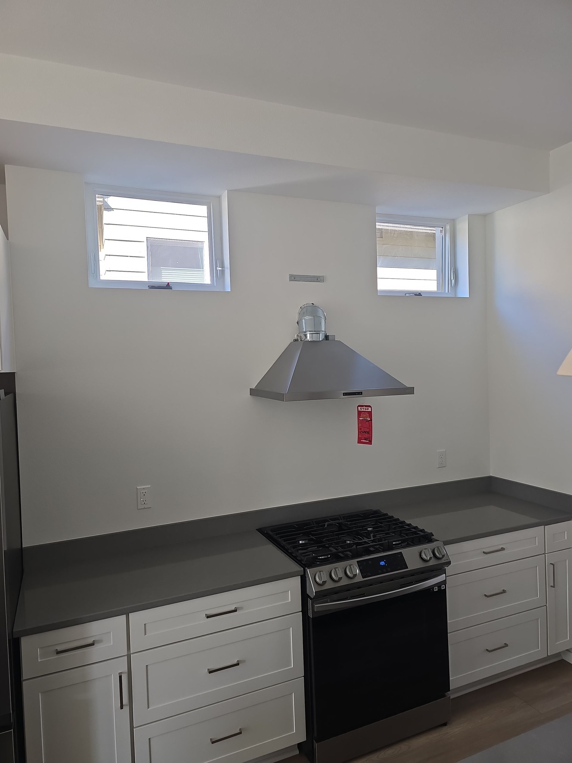 Modern kitchen with gray countertops, white cabinets, black stove, and stainless steel range hood beneath two small windows