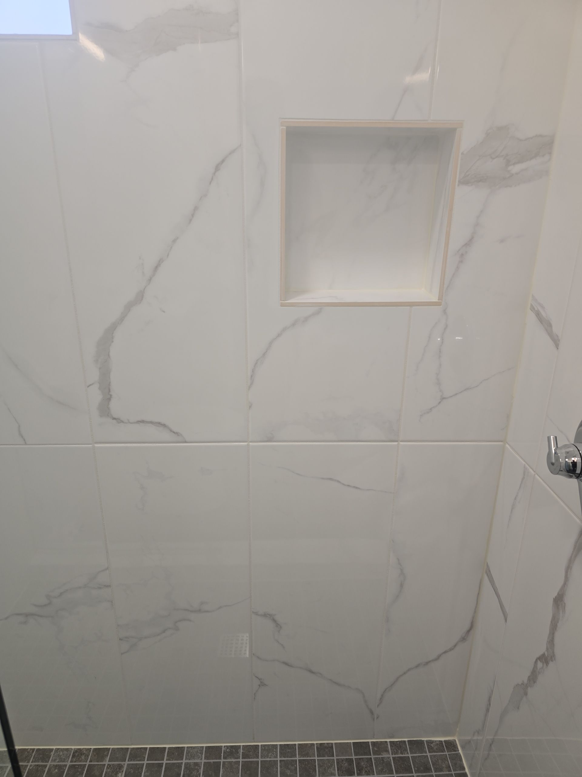 White marble-tile shower wall with built-in niche and chrome fixture, viewed straight on
