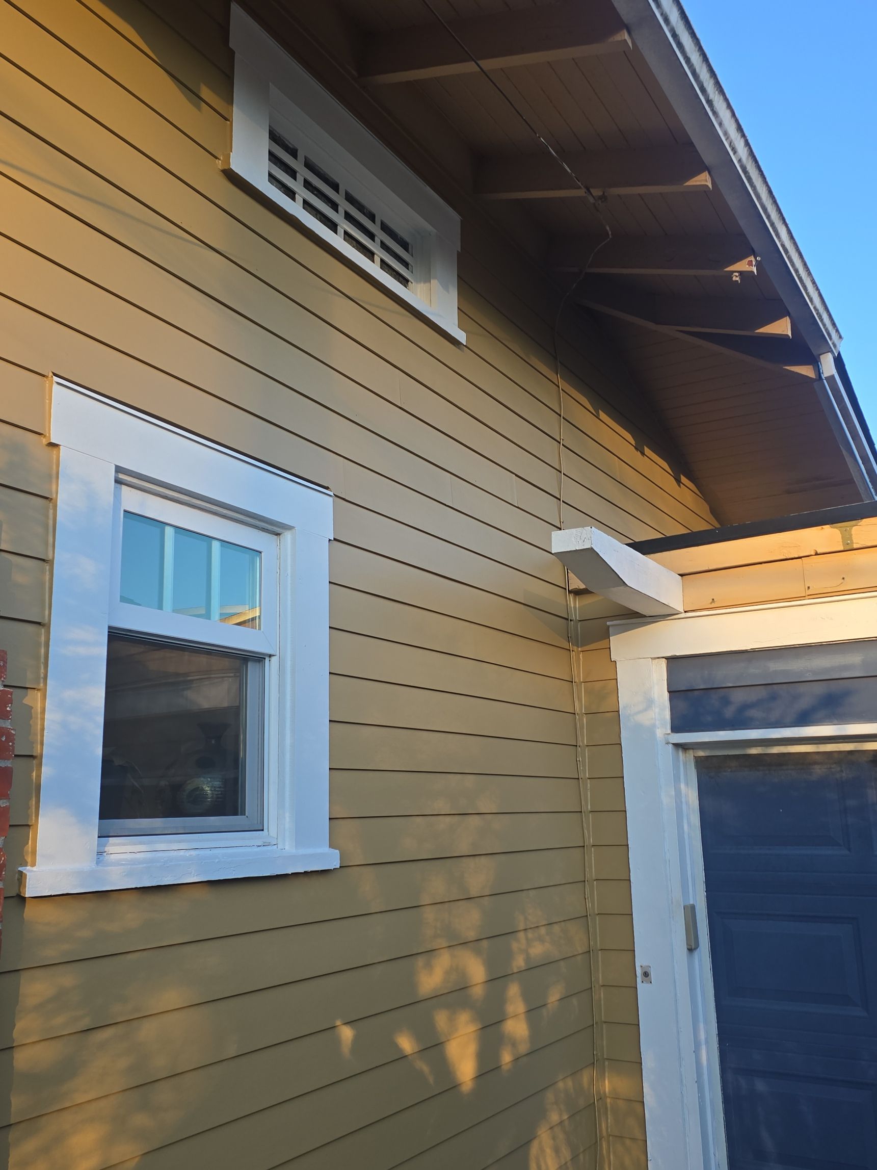 Yellow house exterior with white-trimmed window and blue garage door in sunlight