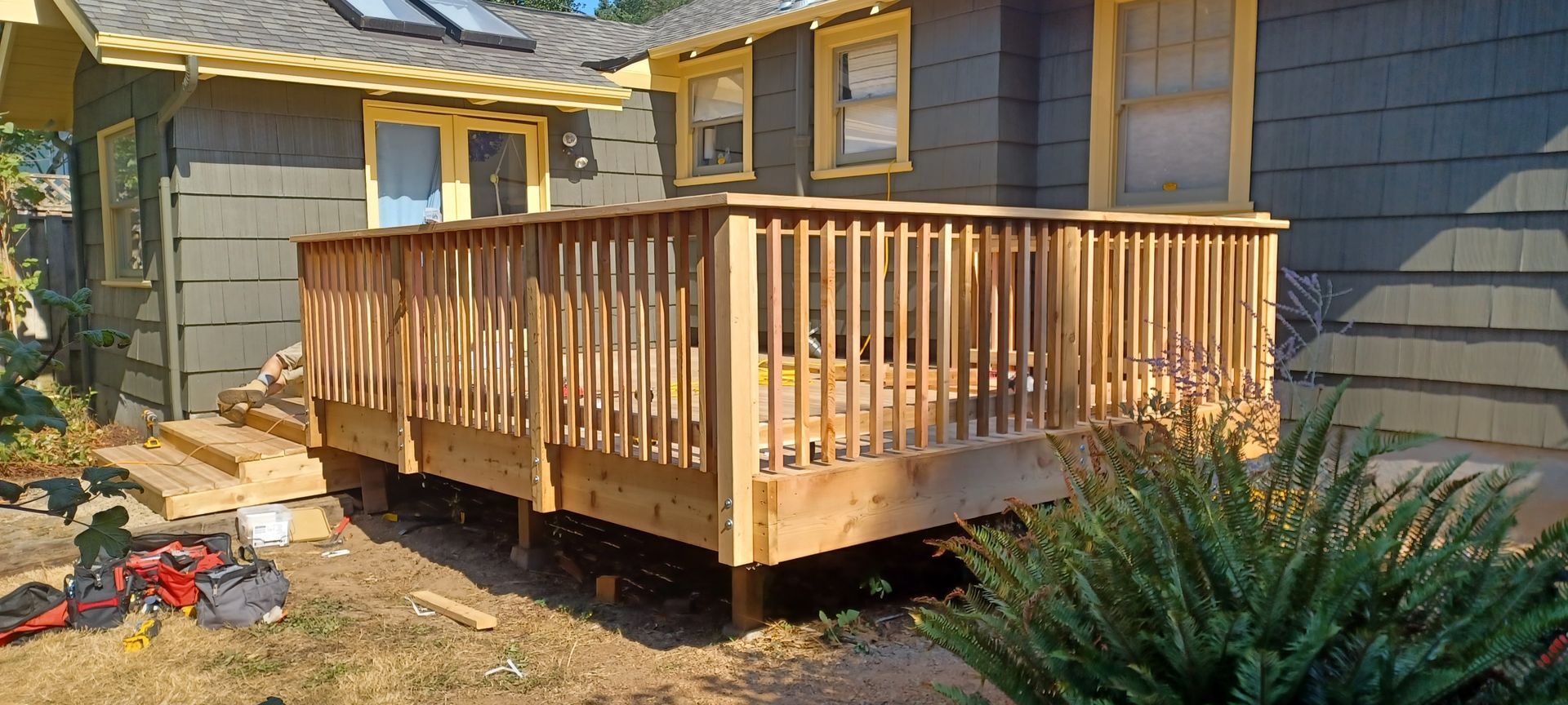 Wooden deck attached to a gray house with yellow trim, viewed from the yard.