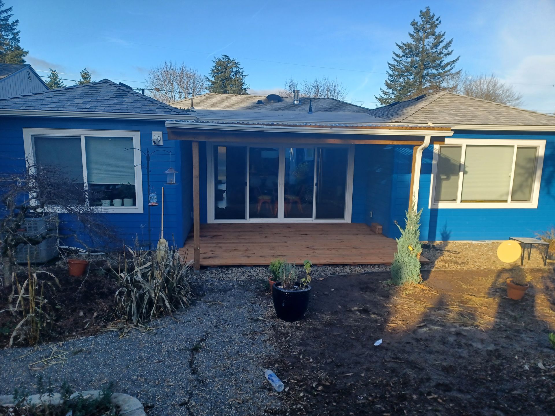 Blue house exterior with a covered front porch, gravel yard, and potted plant in front
