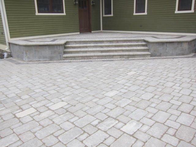 A brick driveway with stairs leading up to a green house.