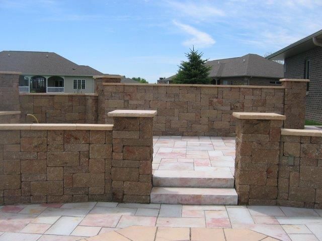 A stone wall with stairs leading to a patio in front of a house.