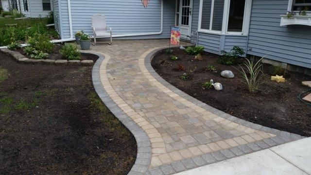 A brick walkway leading to a house with a chair in the background.
