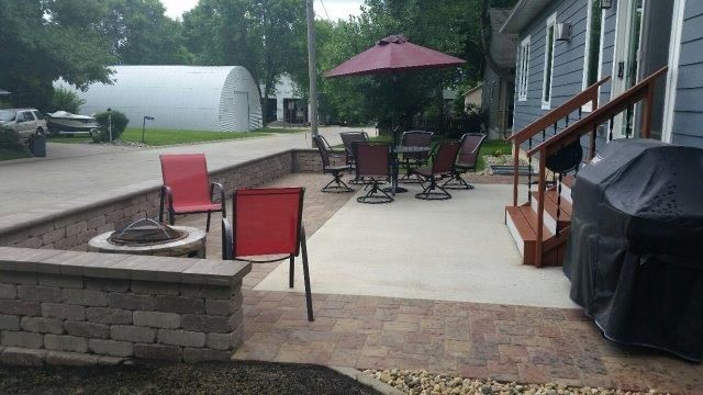 A patio with a fire pit , tables and chairs and an umbrella.
