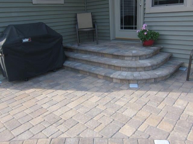 A weber grill sits on a patio next to a set of stairs
