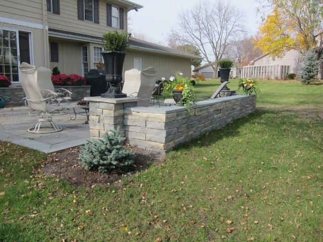 A patio with chairs and a stone wall in front of a house.