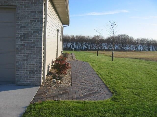 A brick walkway leading to a house next to a lush green field.
