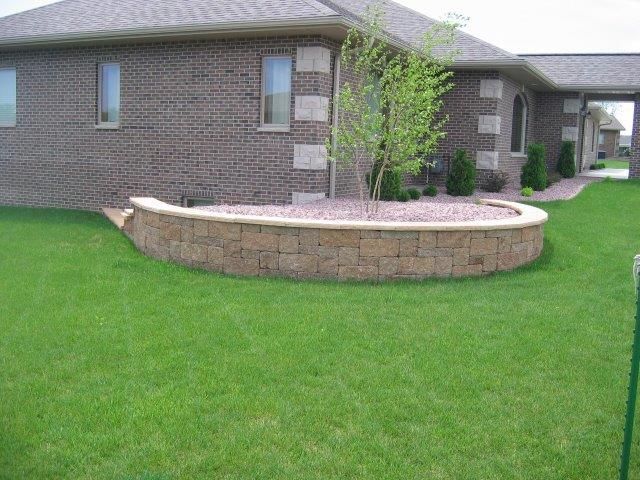 A brick house with a curved stone wall in front of it.