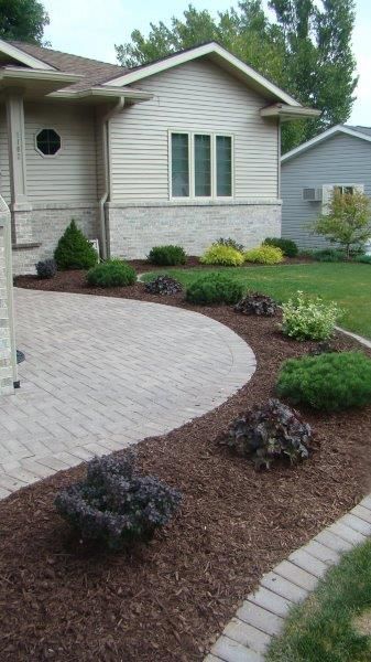 A house with a brick walkway leading to it and a lush green yard.