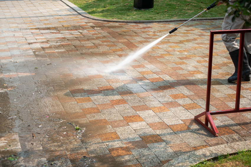 A man is using a high pressure washer to clean a brick driveway.
