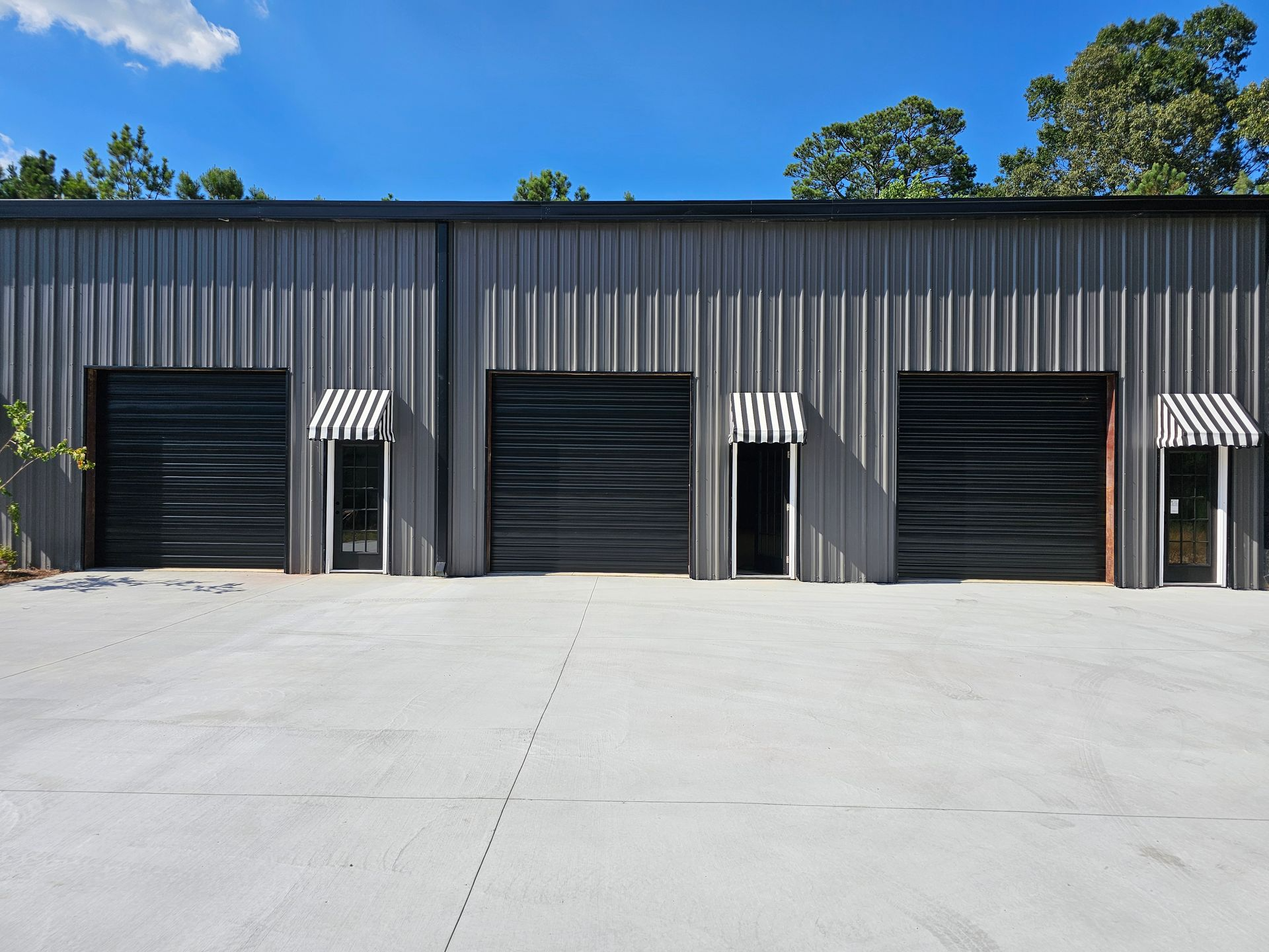 A row of metal buildings with black garage doors and awnings.