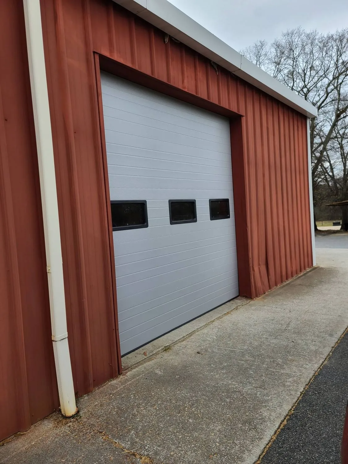 A red building with a white garage door and a white pipe.