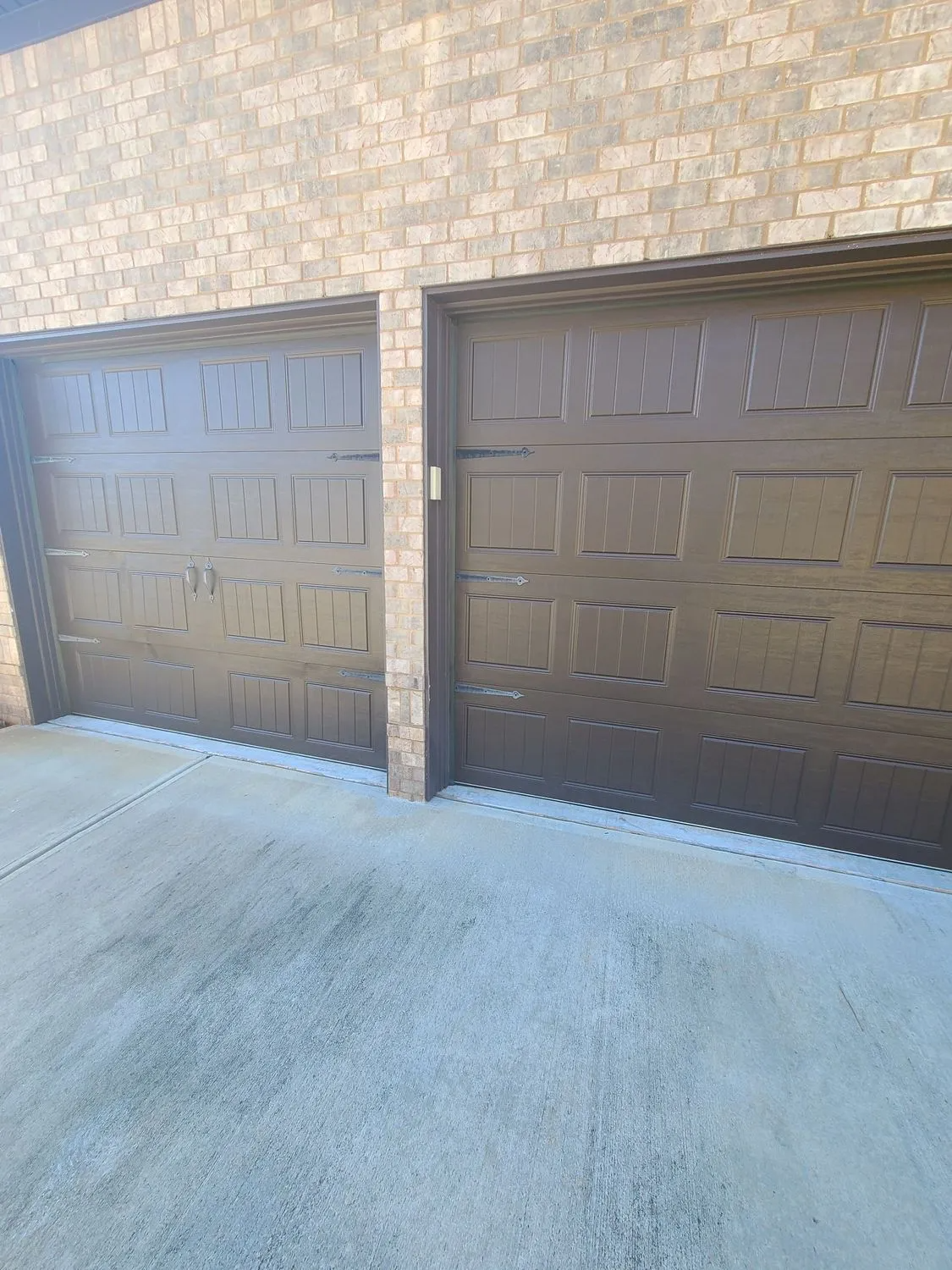 Two brown garage doors are sitting next to each other on a brick building.