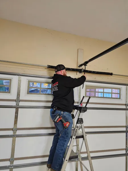 A man is standing on a ladder fixing a garage door.