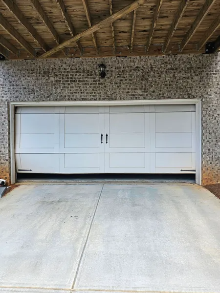 A white garage door is open to a concrete driveway under a wooden roof.