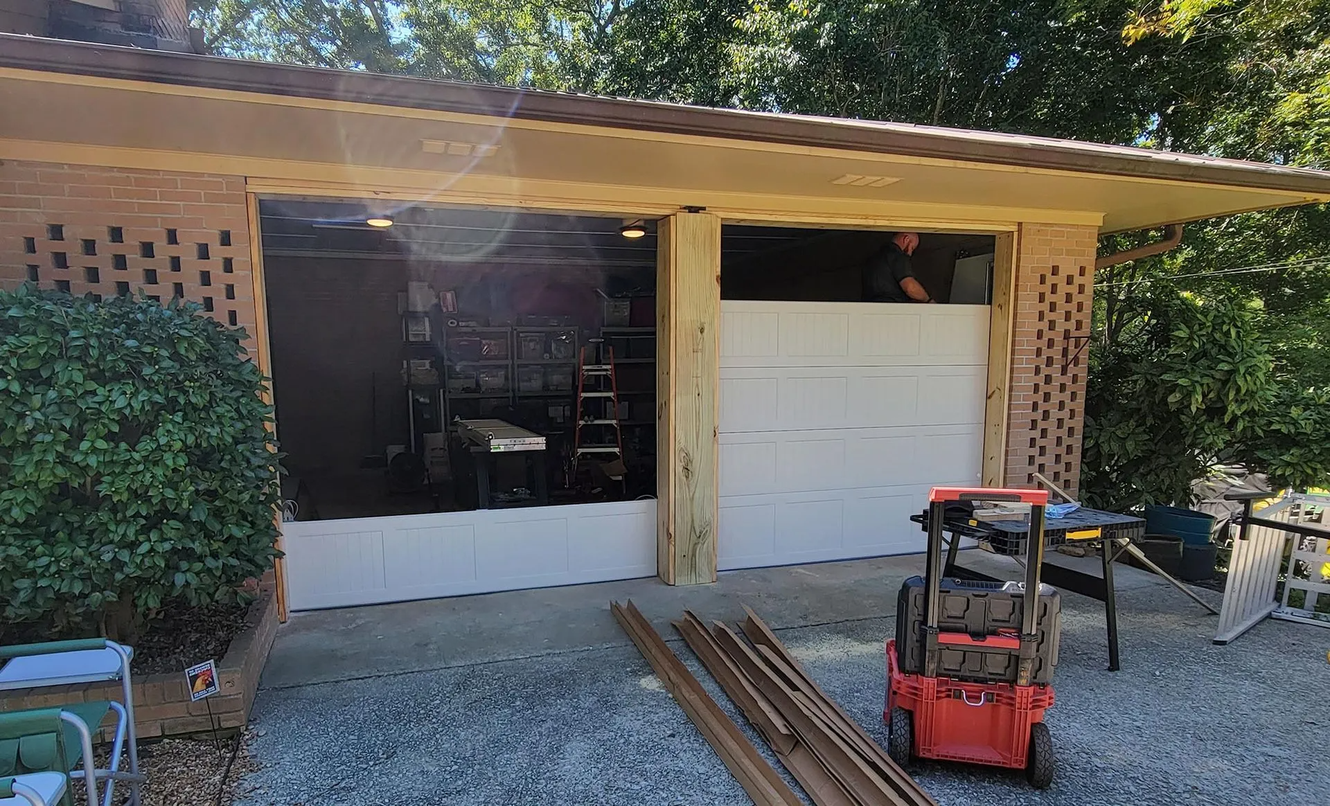 A man is working on a garage door in a driveway.