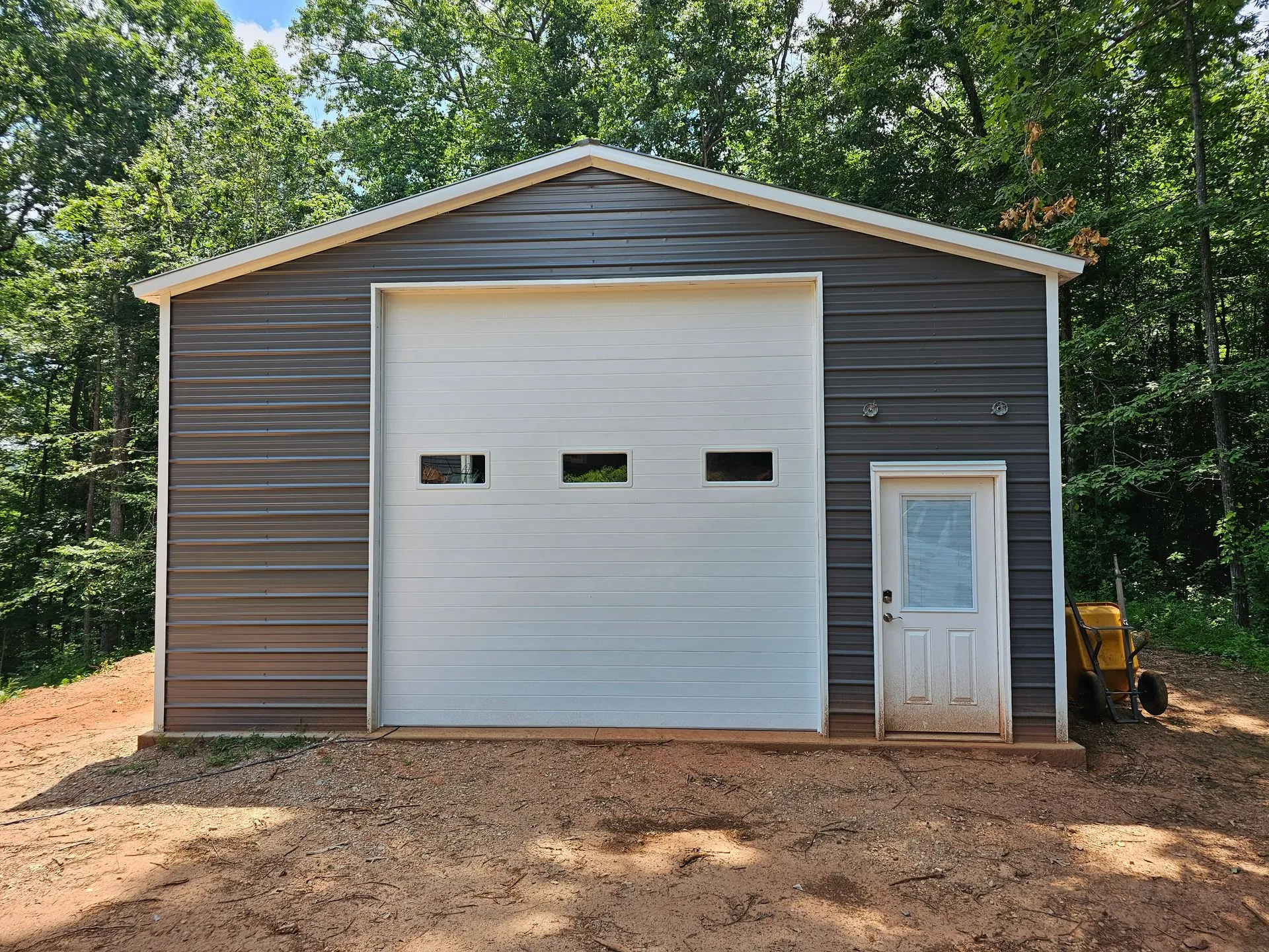 A garage with a large white garage door is sitting in the middle of a dirt field.