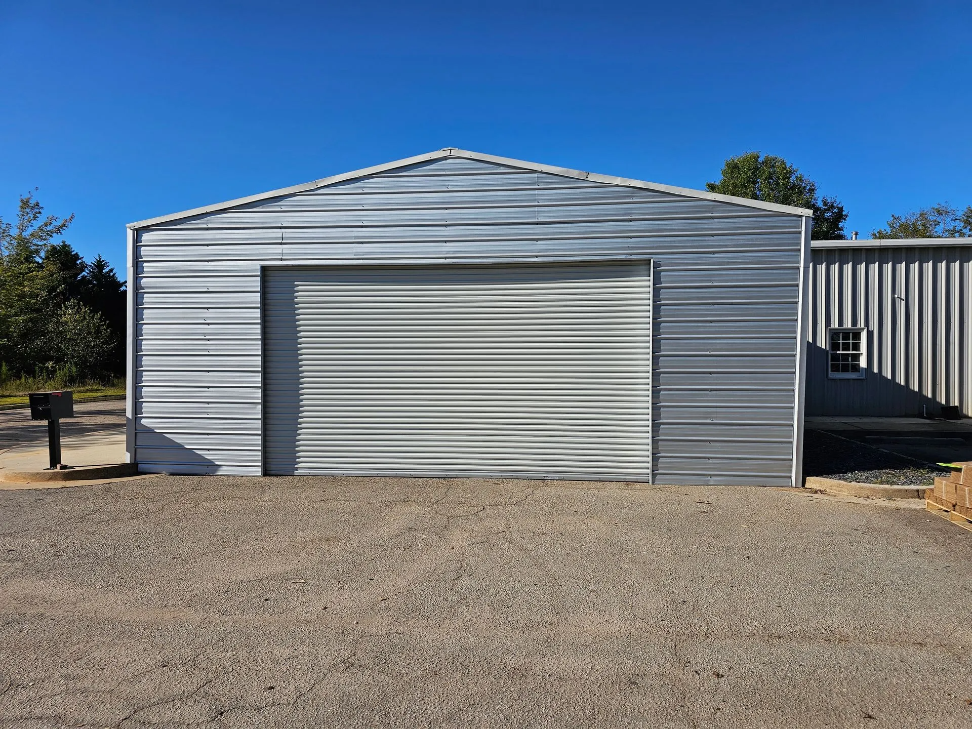 A metal garage with a roller door is sitting on top of a gravel driveway.
