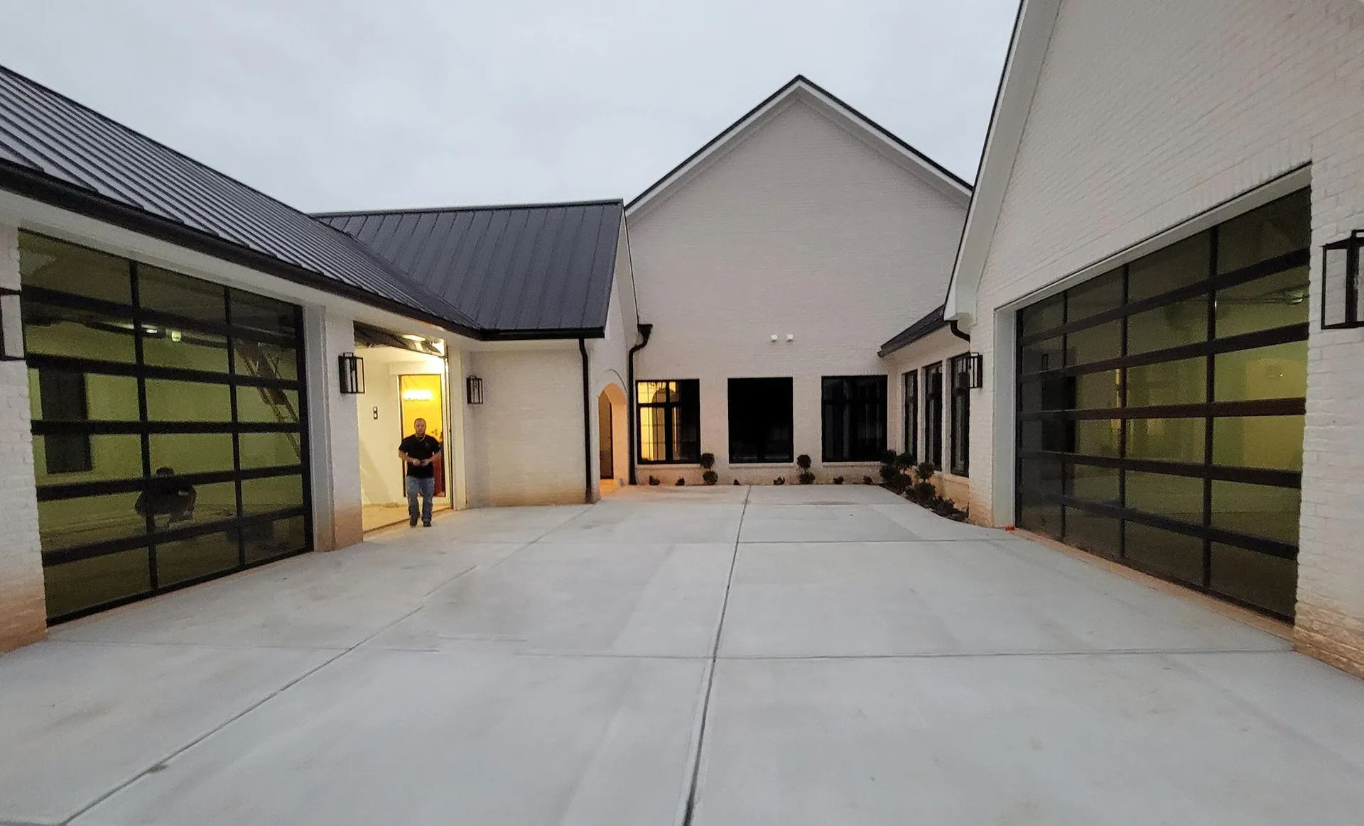 A man is standing in front of a large house with a lot of garage doors.