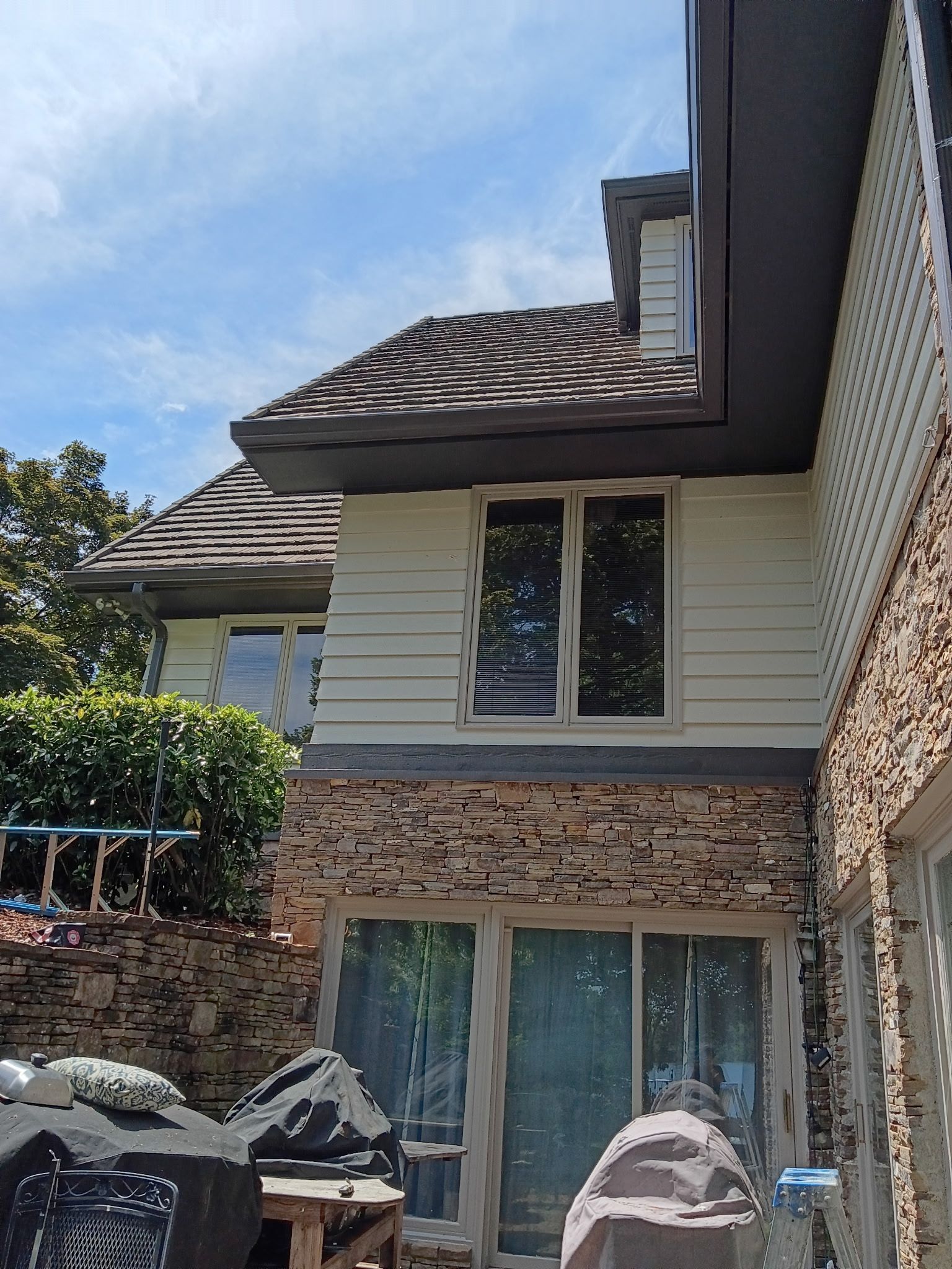 Two-story stone and siding house with a tiled roof, sliding glass doors, and a backyard patio under a blue sky