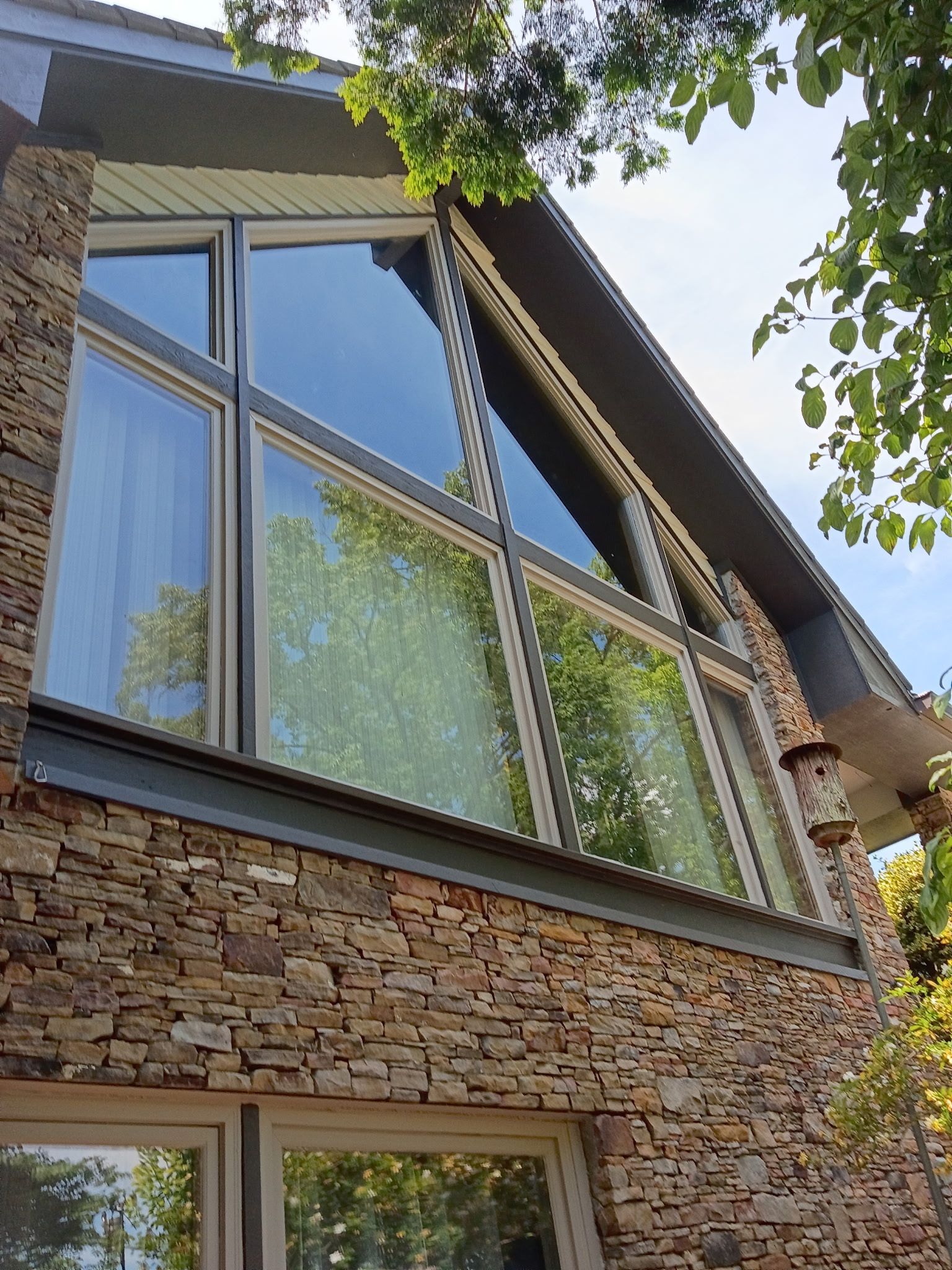 Low-angle view of a stone house facade with large triangular windows and tree branches overhead