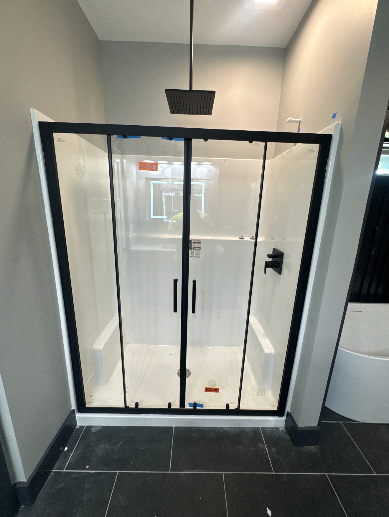 Small glass shower enclosure with black frame in a tiled bathroom hallway.