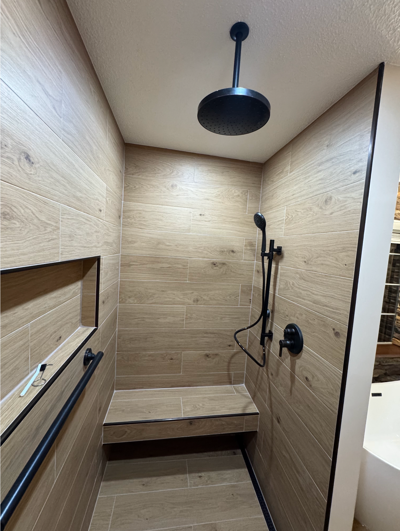 Small tiled shower stall with a bench, handheld shower, and overhead rain showerhead.