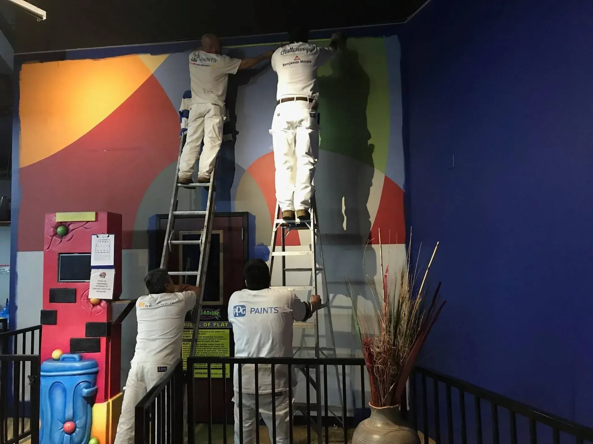 Four painters on ladders, painting a colorful wall.