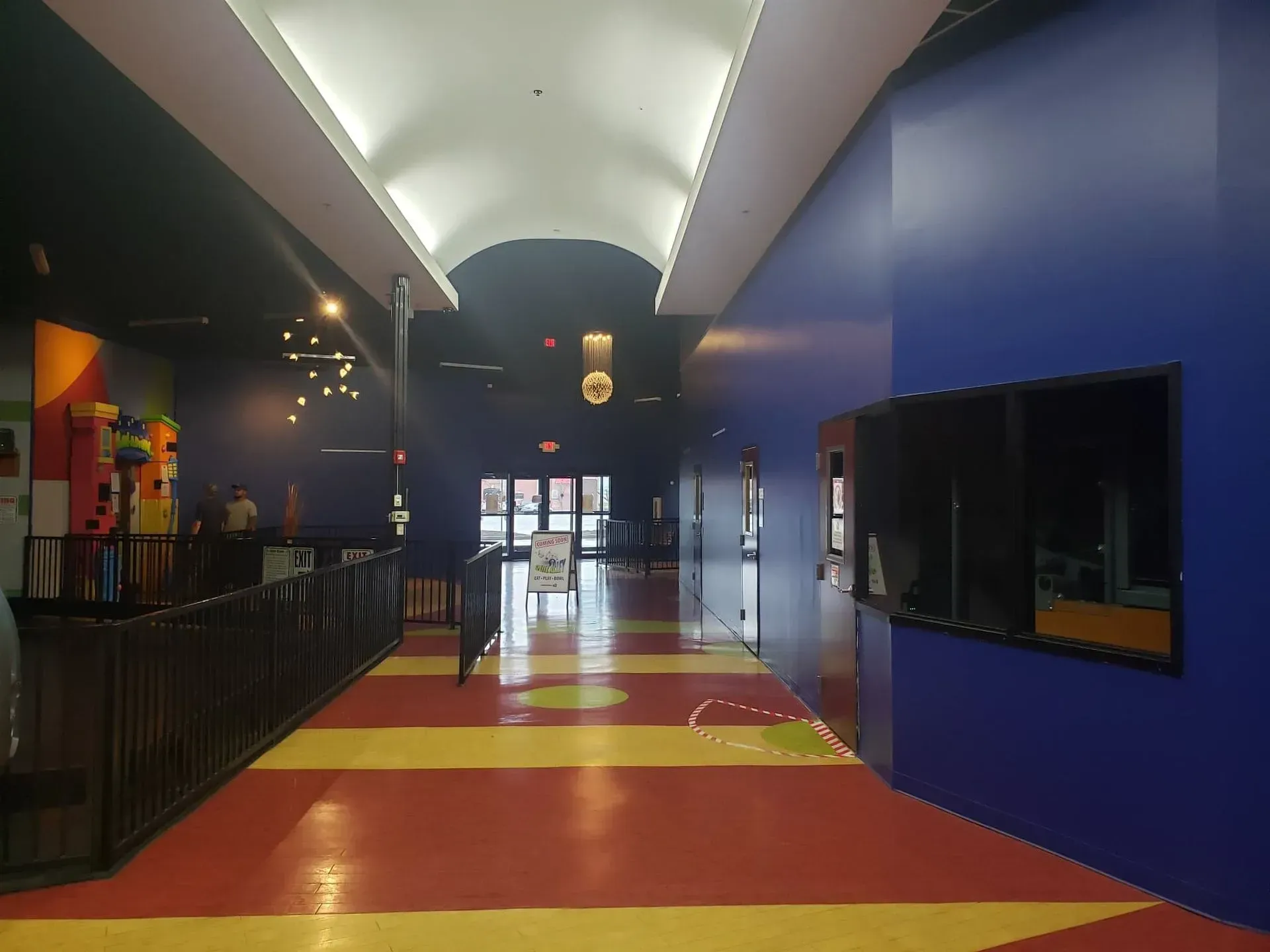 Long hallway with blue, red, and yellow flooring, blue walls, and a white arched ceiling.