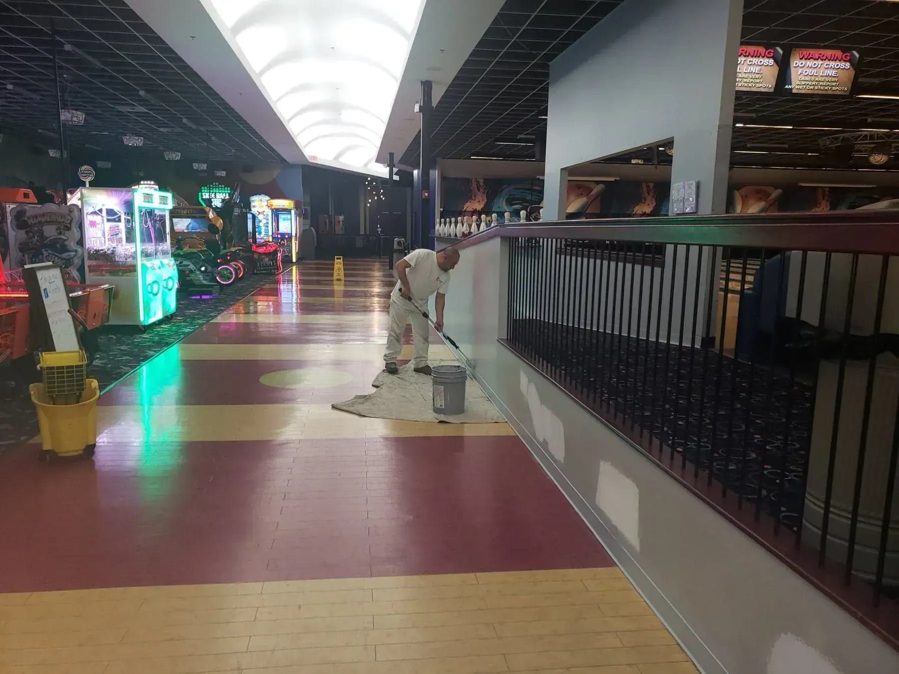 A person painting a wall in an arcade with red and tan floors. Games are on the left.