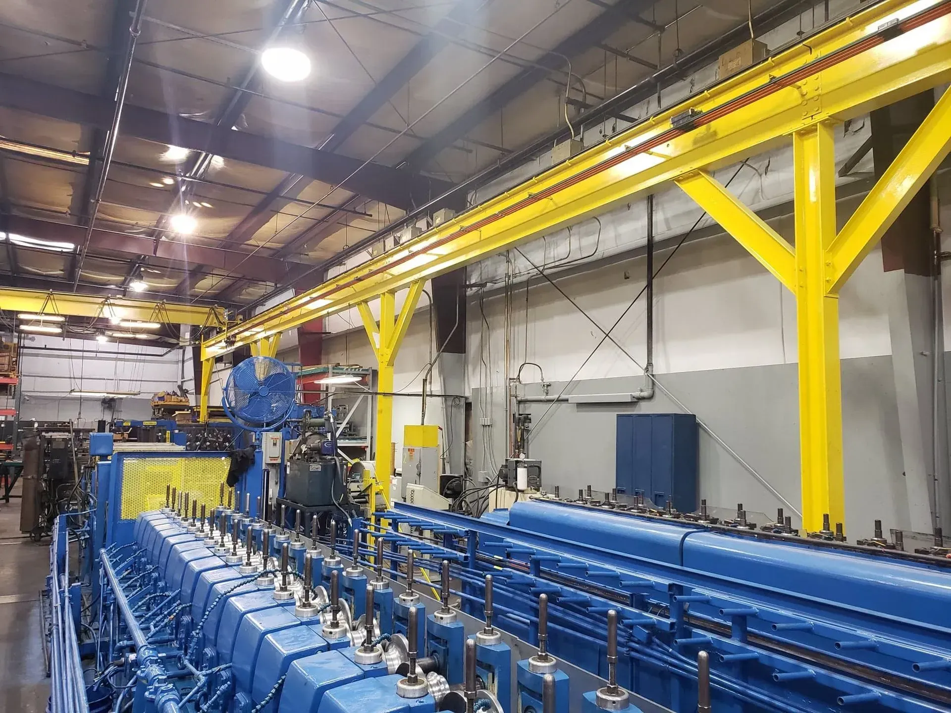 Blue industrial machine in a factory with yellow overhead support beams.