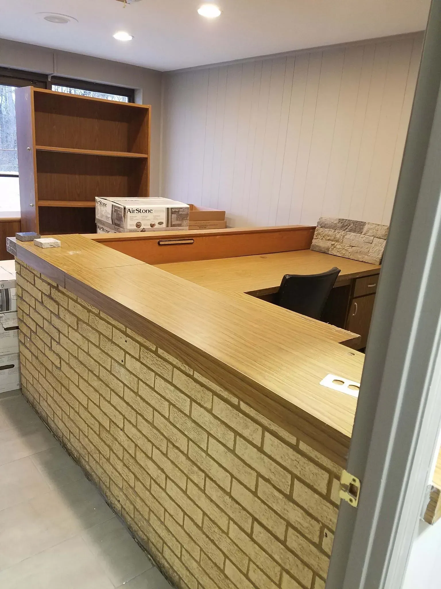 Reception desk with brick facade, wooden countertop, and built-in shelves.