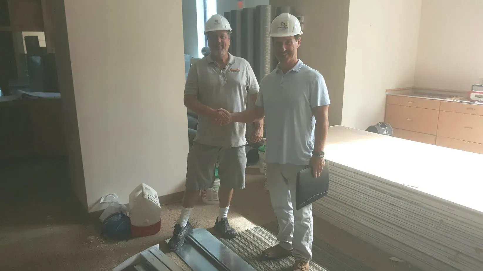 Two construction workers in hard hats shaking hands in a building interior.