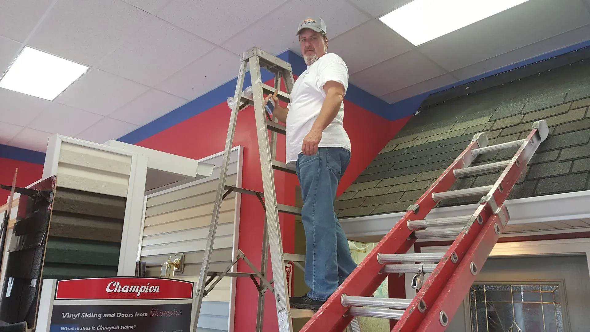 Man on a ladder inside, near a display of roofing and siding.
