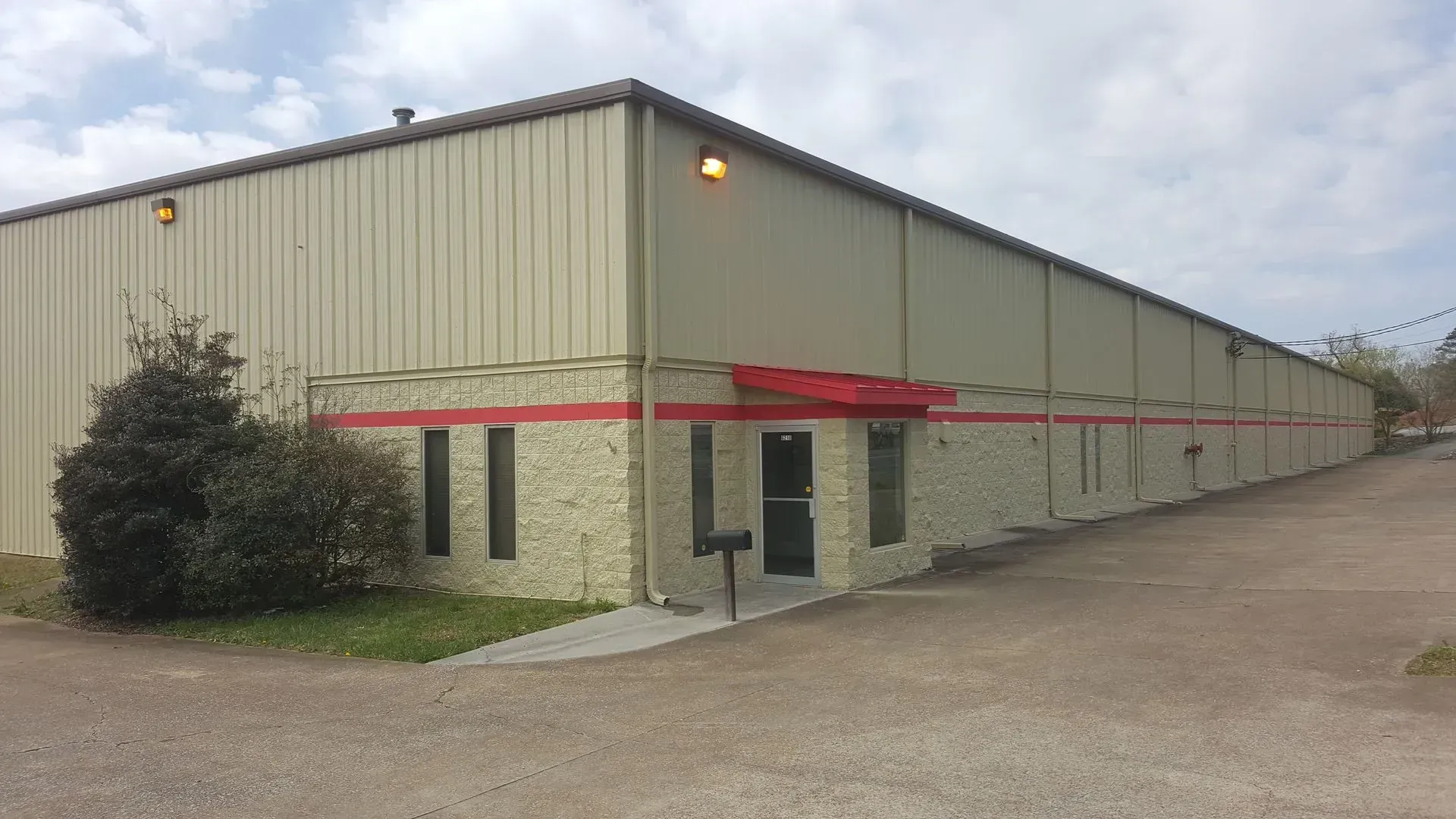 Tan industrial building with red stripe, small entrance, and cloudy sky.