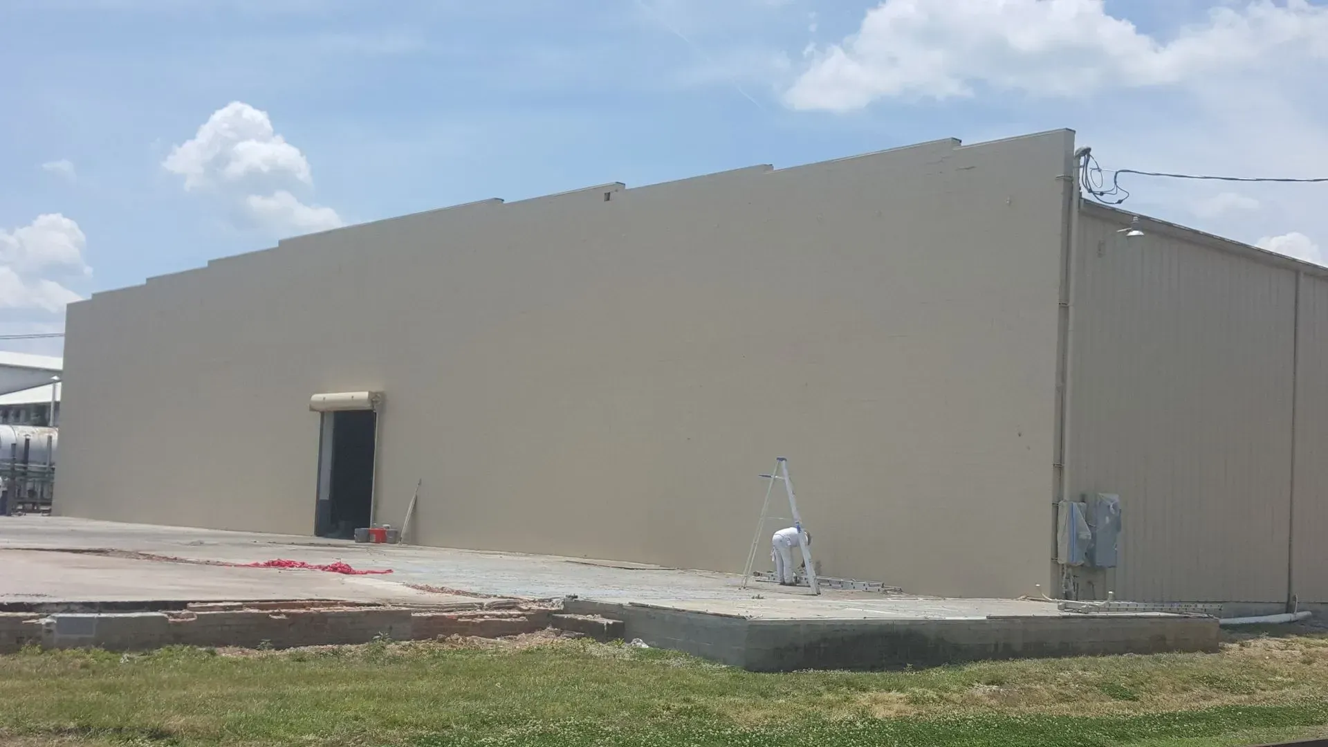 Beige industrial building with a door, set against a cloudy blue sky.