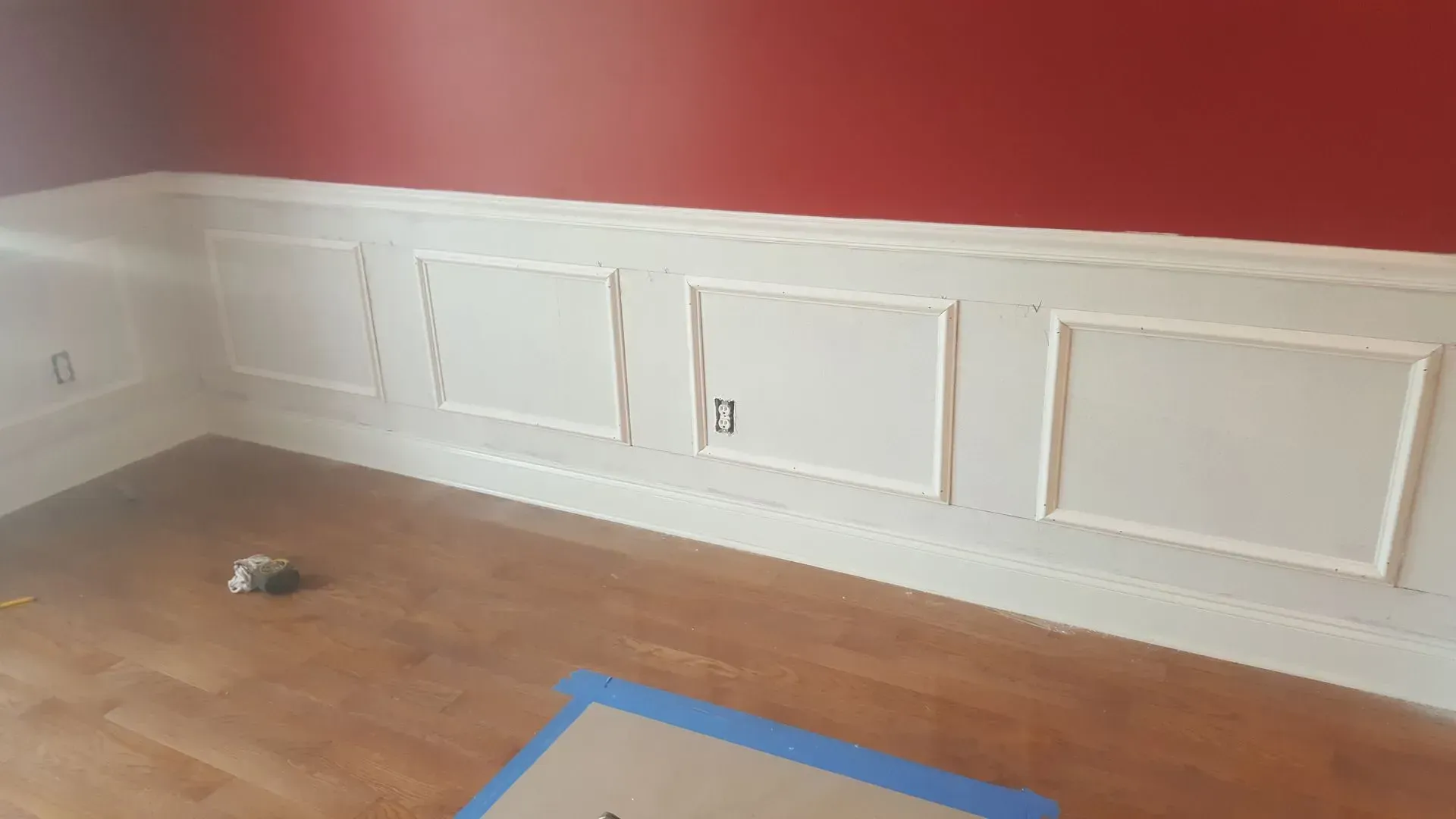 White wainscoting with red wall above, hardwood floor, and outlet in wall.