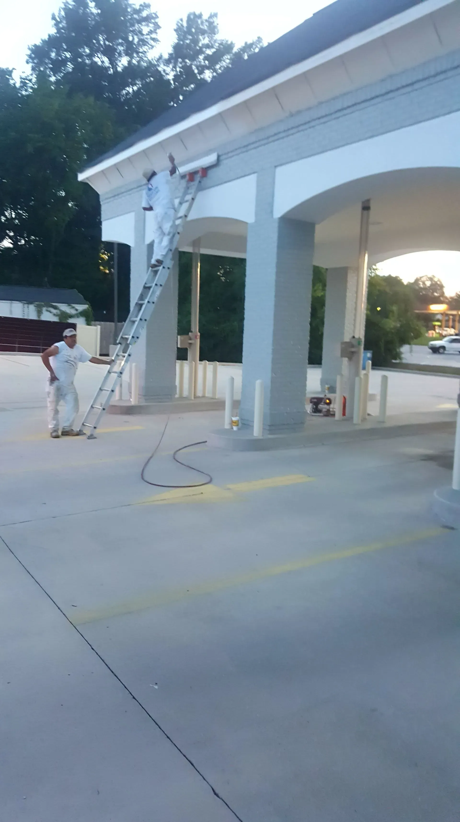 Man painting building exterior using a ladder at gas station.