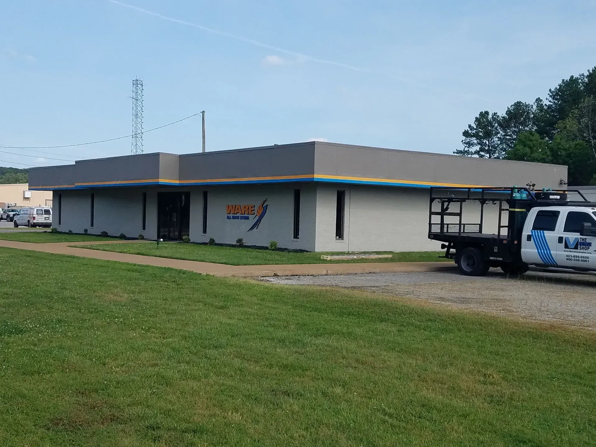 Gray commercial building with a logo; a work truck is parked nearby.