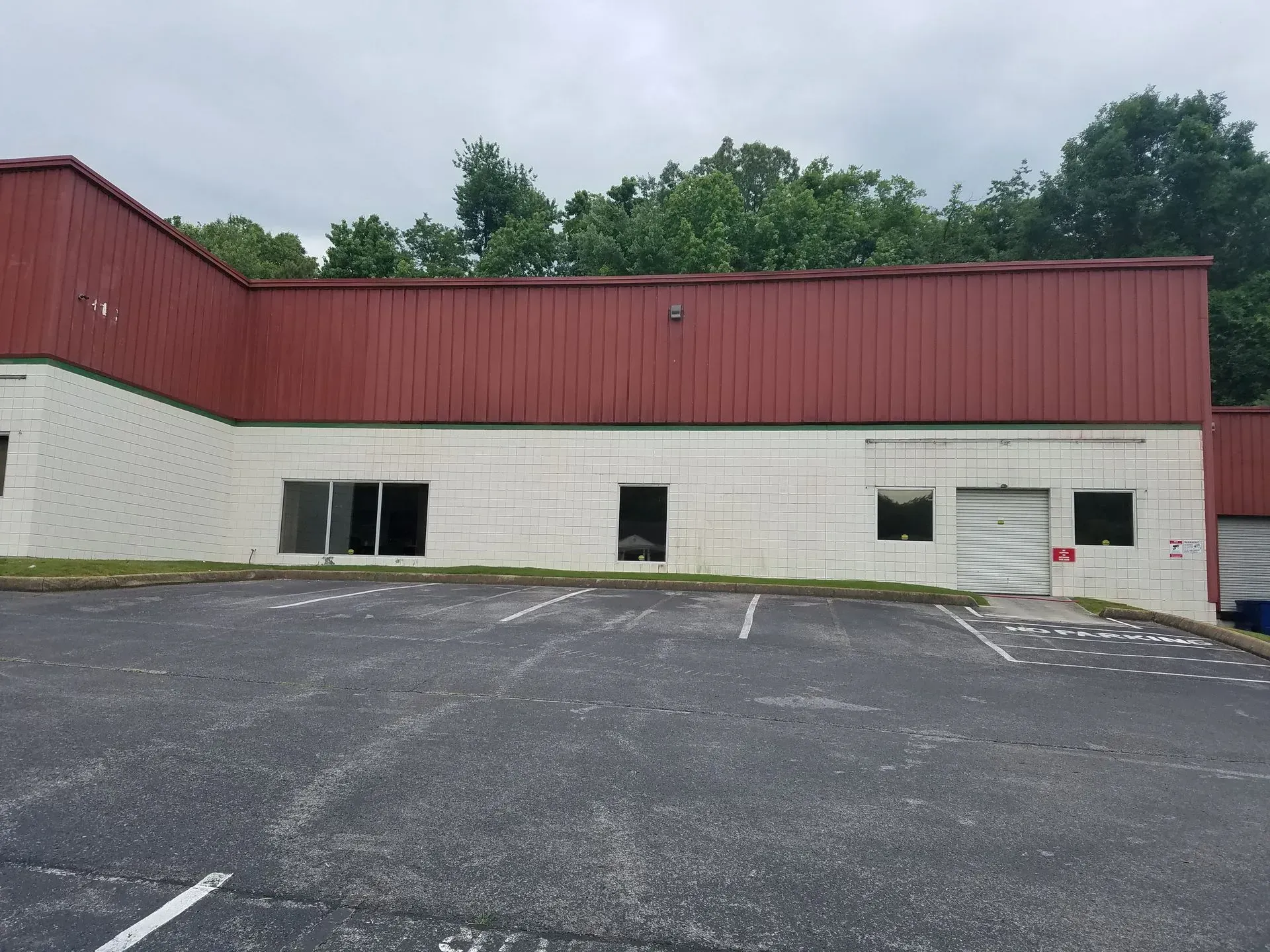 Building with red roof and white brick facade, broken windows, and cracked asphalt parking lot.