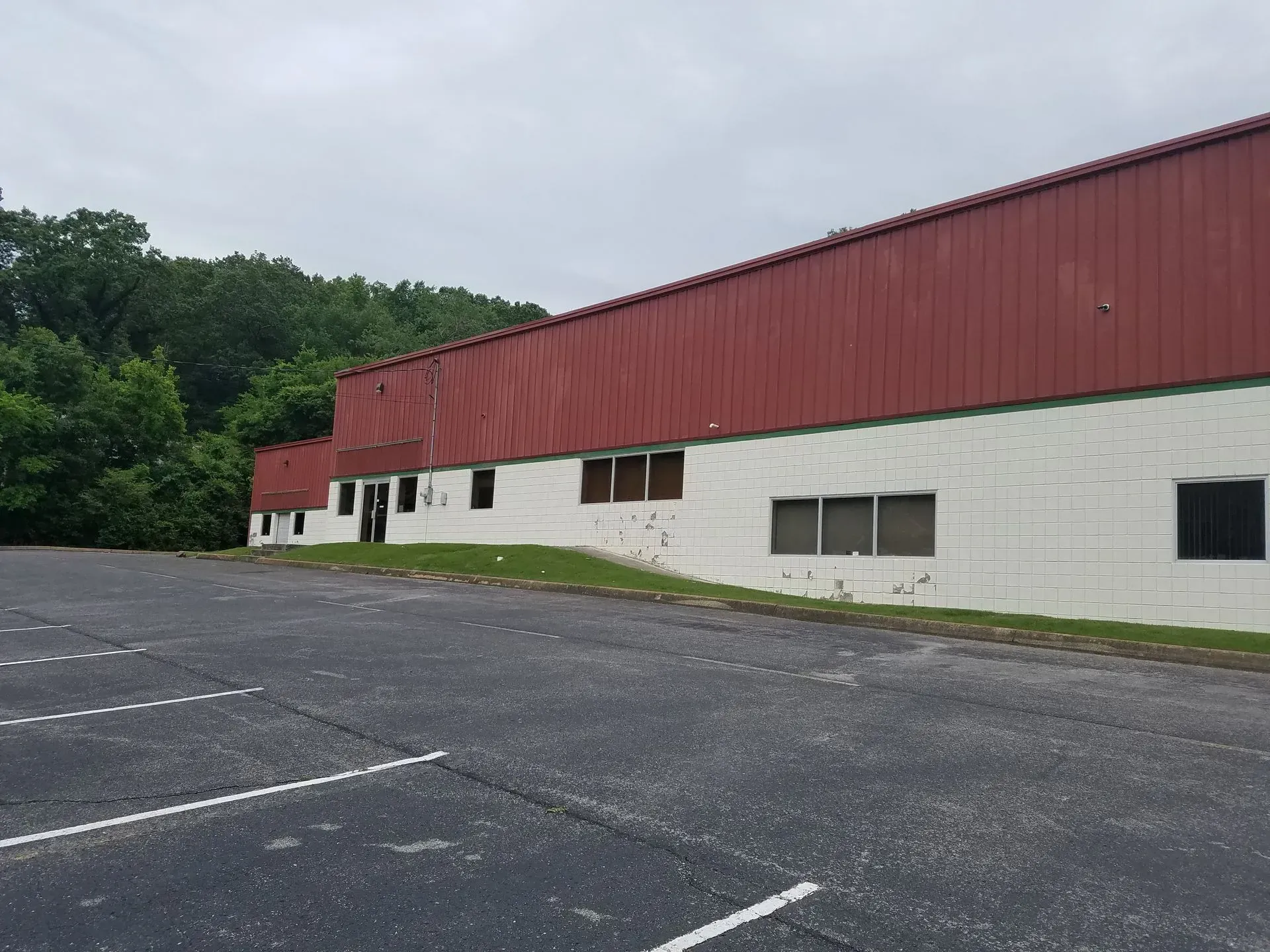 A low, red-roofed commercial building with white walls, set back from a paved parking lot and trees.