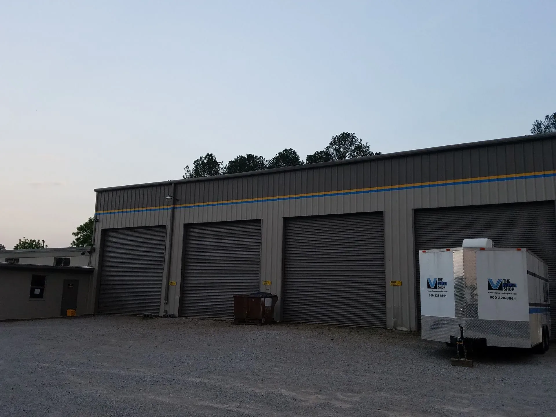 Three garage doors with metal siding; a trailer is parked on gravel.