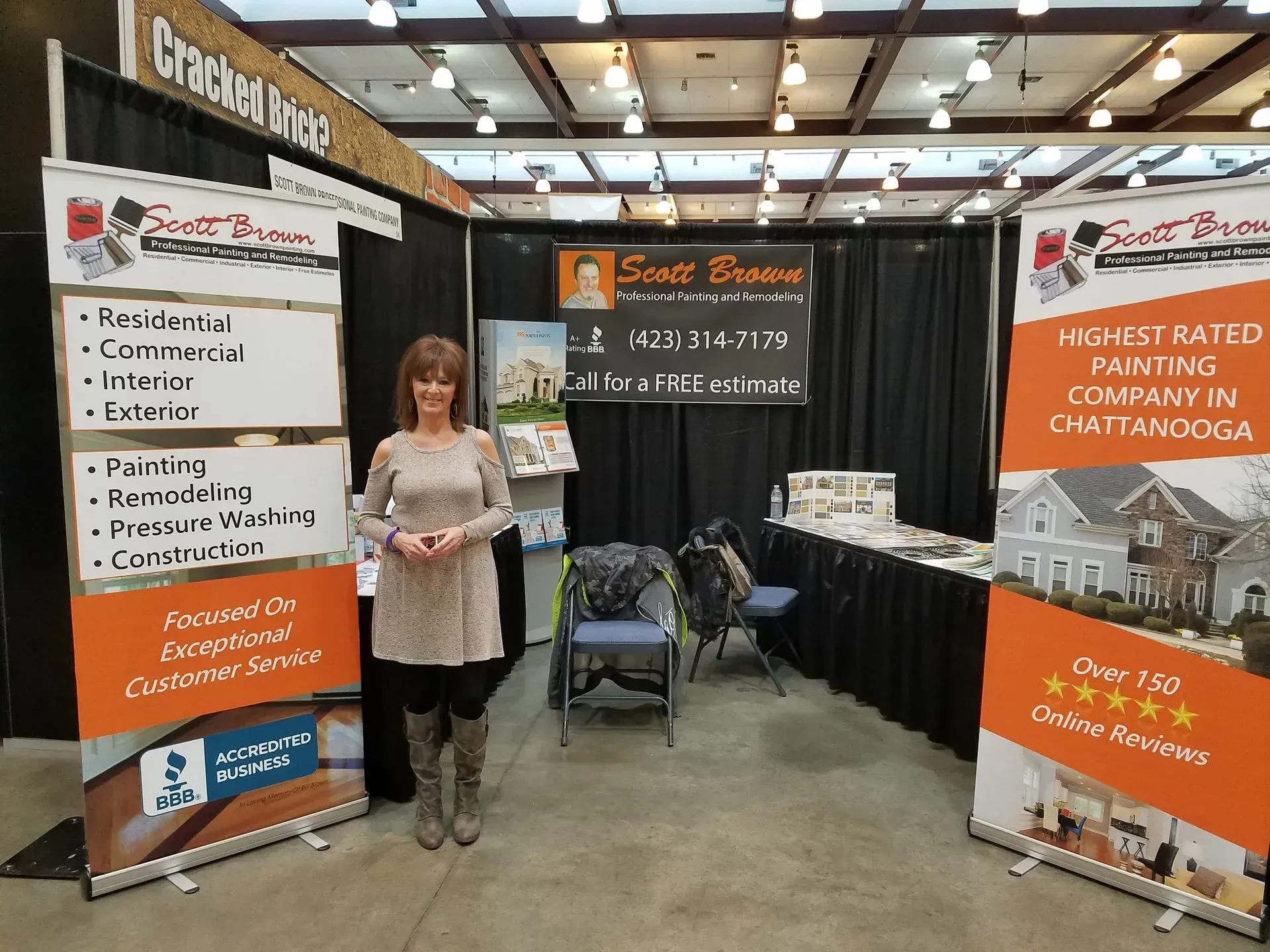 Woman stands in a booth promoting Scott Brown painting services.  Includes signs, contact info, and examples of work.