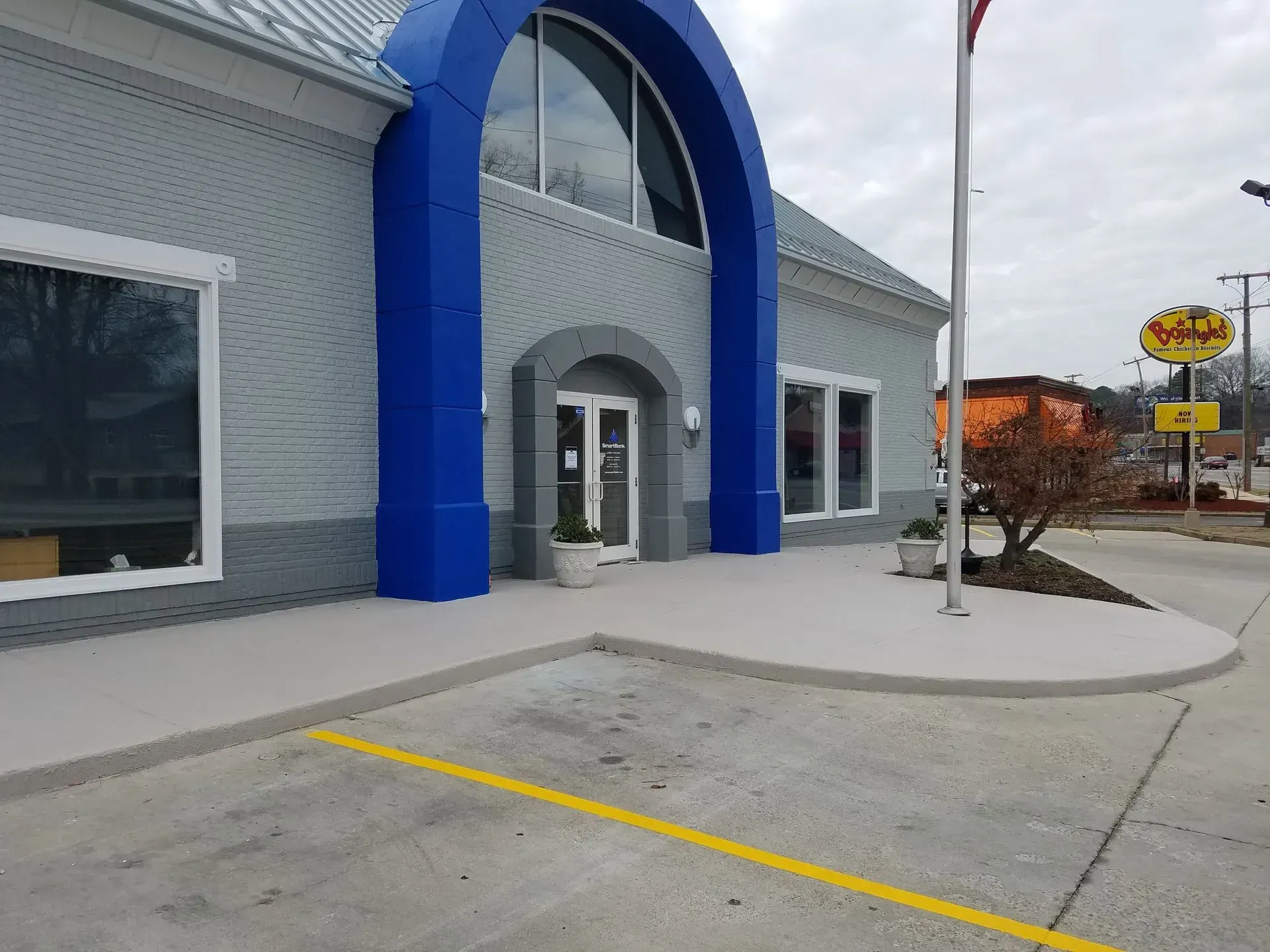Gray building with blue archway entrance, white windows, and parking lot. A sign for 