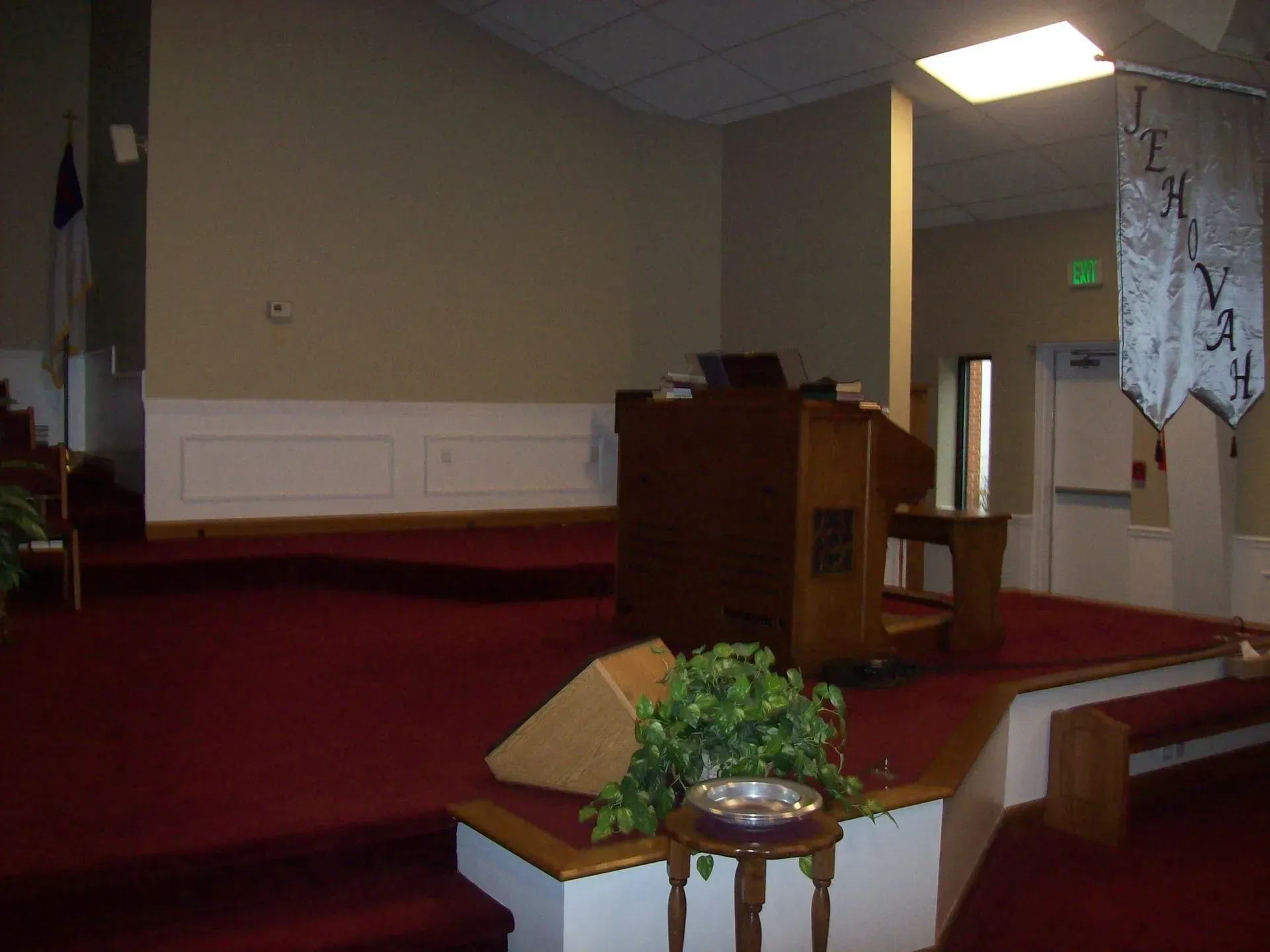 Interior view of a church stage with a podium, red carpet, and decorative plants.