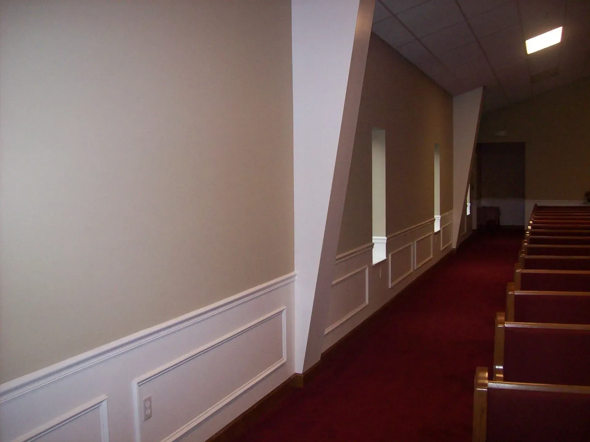 An interior of a church with red carpet, rows of pews, and cream-colored walls with white wainscoting.