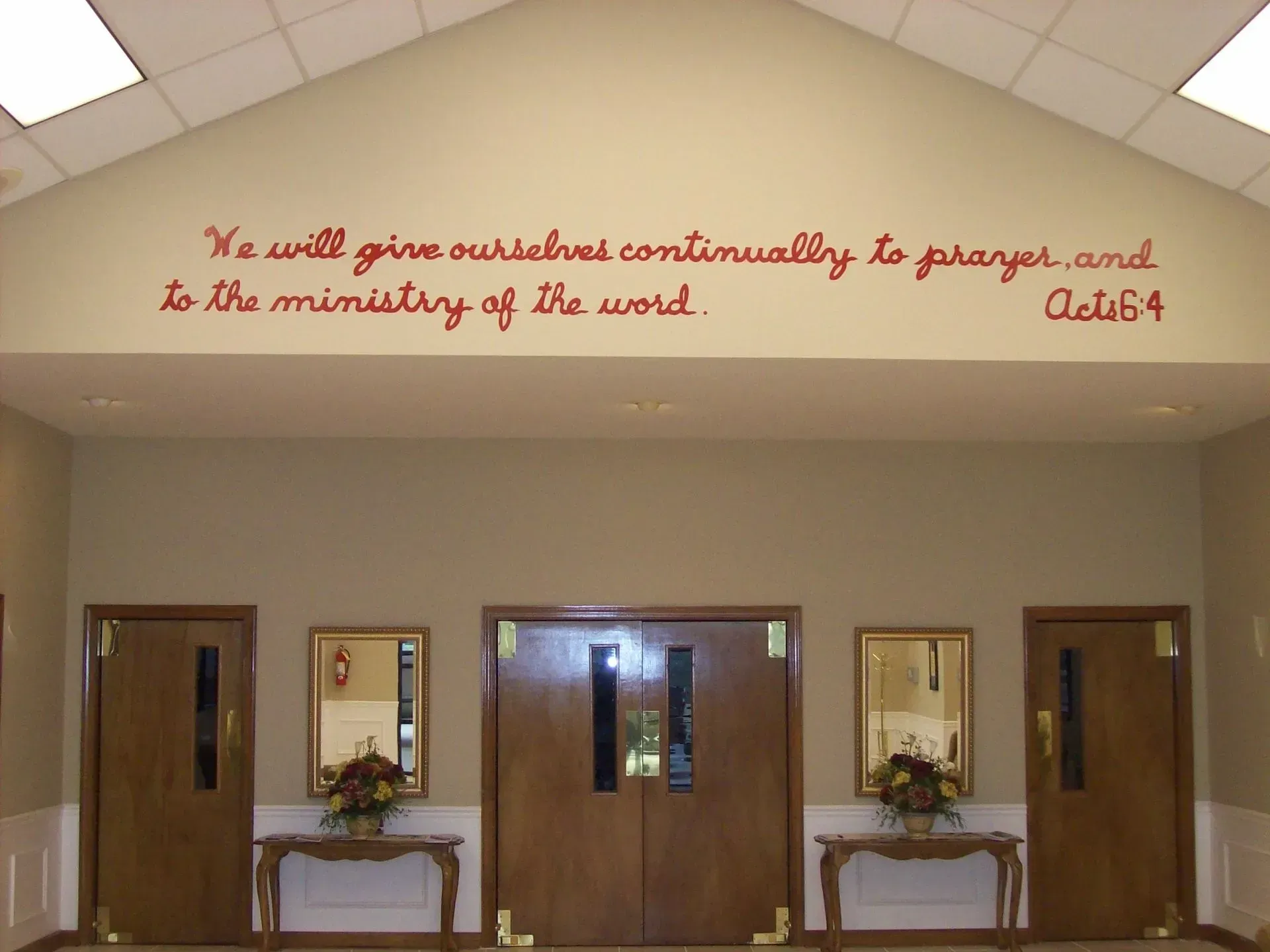 Red text on a beige wall in a church entrance: Bible verse 
