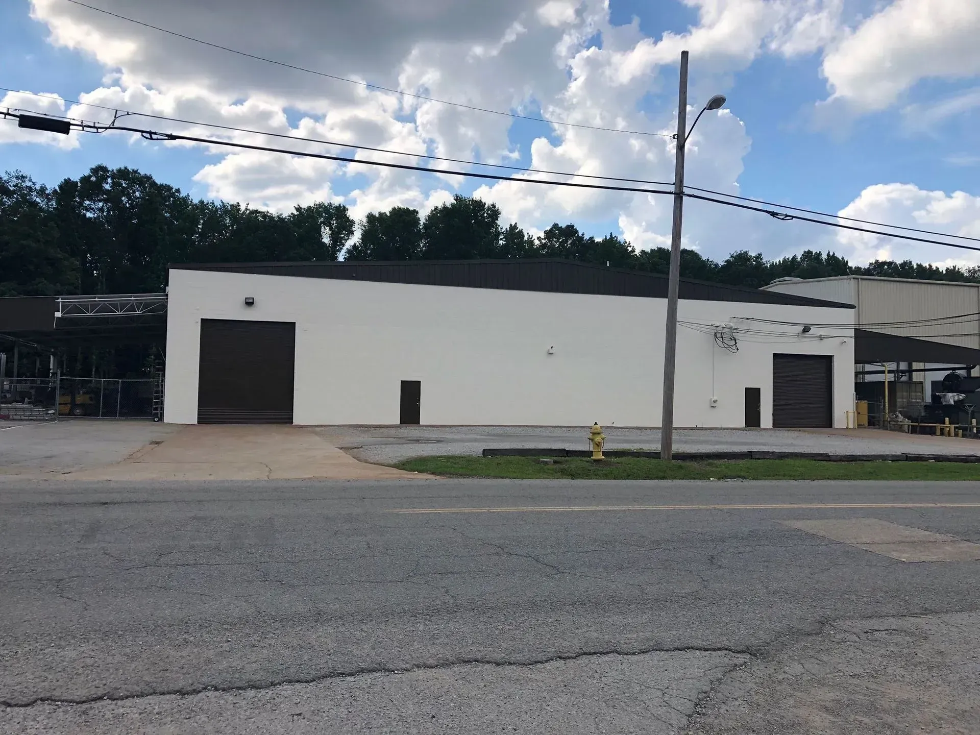 A white commercial building with two garage doors faces a gray street under a cloudy sky.